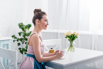 attractive elegant young woman sitting at table, smiling and drinking coffee