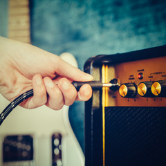 Guitar electric amplifier. Rock overdrive effect. Hand is plugging a cable into amp jack. Max volume knob. Shallow depth of field