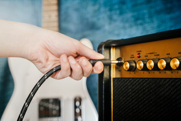 Guitar electric amplifier. Rock overdrive effect. Hand is plugging a cable into amp jack. Max volume knob. Shallow depth of field