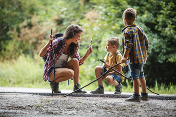 Mother and her little sons hiking trough forest .They using magnifying glass and looking at insects.