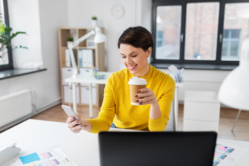 business, technology and user interface design concept - smiling businesswoman or ui designer using smartphone and drinking takeaway coffee from paper cup at office