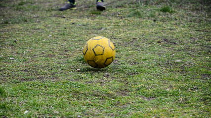 Yellow soccer ball rolling on the grass, a game of football in the yard.