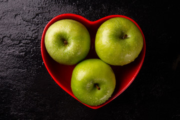 green apples into heart bowl on table close up.