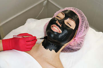 Beautician apply black moisturizing mask on girl's face. Skin repairing procedure