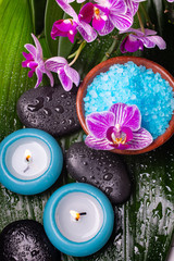 bowl with lavender-scented bath salt, orchid, massage stones, covered with water drops, and scented candles.
