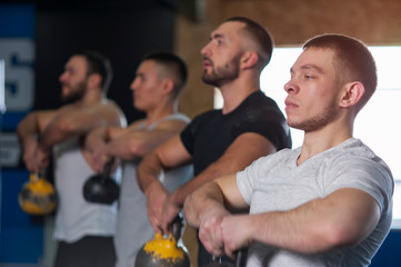 Male Focused Friends Lifting Kettlebells During Workout Session in Gym