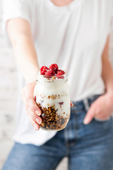 Jar of yogurt granola parfait in girl's hand. Healthy balanced diet meal. Trendy food culture