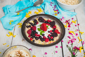 granola, fresh, nutritious breakfast with the addition of natural yoghurt, fresh and frozen fruit, and mint leaves,  on a white table decorated with spring flowers