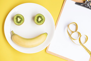 Sliced kiwi , banana and centimeter on a white plate on the yellow background. Diet concept. 