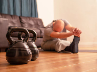 Fitness concept, kettlebell in focus, bold man doing strech excercise on a floor out of focus, workout at home.