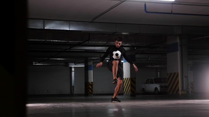 Underground parking lot. A soccer man training his football skills. Balance the ball on his knee