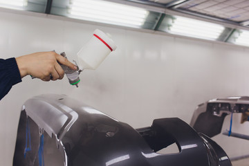 worker painting a car black blank parts in special garage, wearing costume and protective gear.