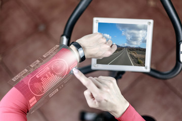 Techno concept: a girl on a stationary bike is watching an electronic screen fitness bracelet
