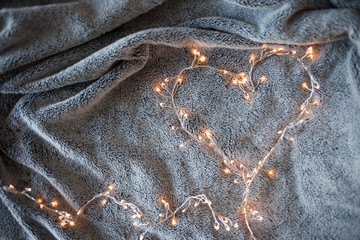 Garland heart with glowing lights in the background of a fluffy grey blanket