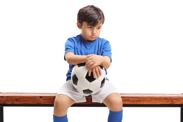 Sad little boy with a football sitting on a wooden bench