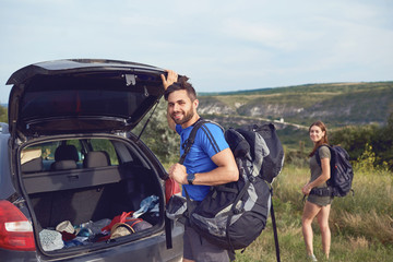 A couple of tourists with backpacks near a car on  nature.