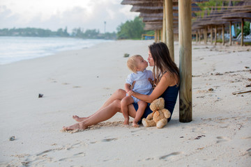 Happy beautiful fashion family, mom and baby, hugging, casually dressed, enjoying the sunrise on the beach in Mauritius