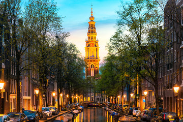 Amsterdam Zuiderkerk church tower at the end of a canal in the city of Amsterdam, Netherlands at night .