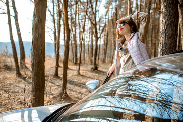 Young woman traveler enjoying nature while traveling by car in the picturesquare forest with lake