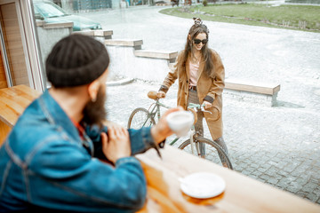Stylish man meeting his girlfriend with bicycle while sitting with coffee near the window at the cafe
