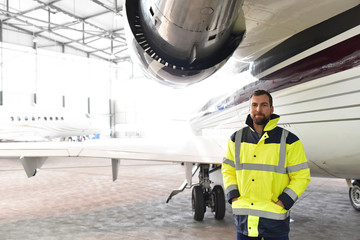 Portrait of an aircraft mechanic in a hangar with jets at the airport - Checking the aircraft for safety and technical function