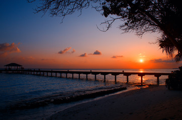 Silhouette of the long pier, bridge, bungalow on the background of a sunset on Maldives Islands. Night landscape
