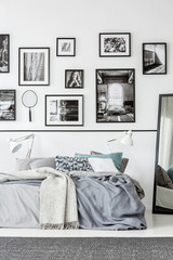 Grey carpet in front of bed and mirror in white and black bedroom interior with gallery. Real photo