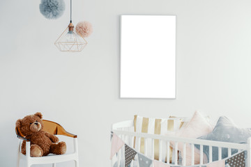 Mockup of empty white poster above cradle in baby's bedroom interior with toy on chair. Real photo