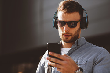 Young man listening to music via headphones and smartphone on the street