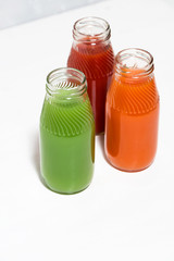 colorful vegetable juices in bottles on white table, vertical top view