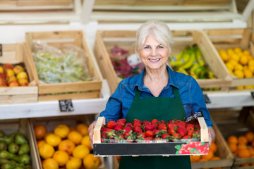 Shop assistant holding box with fresh strawberries in organic produce shop
