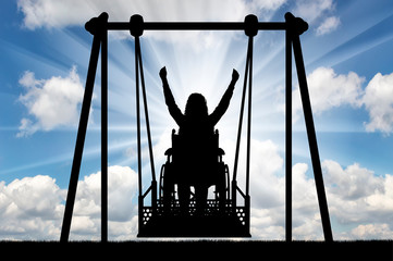 Silhouette of a happy woman is a disabled person in a wheelchair on an adaptive swing for disabled people