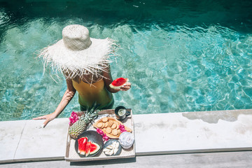 Girl eating fruits in pool on luxury villa in Bali