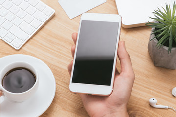 Male hands holding white phone with blank screen on the men table