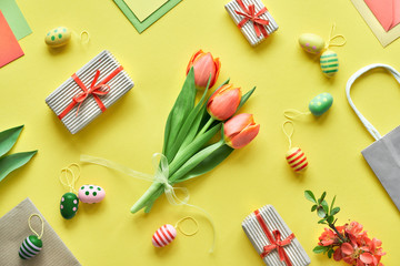 Easter flat lay on yellow paper. Bunch of tulips, gift boxes, decorative eggs and paper bags, geometric diagonal arrangement.