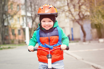 Little cool boy in a helmet and a red vest riding a bicycle with a blue backpack on his back.