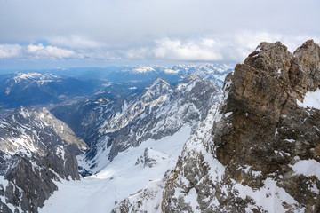 view in the valley from the Zugspitze, the highest mountain of Germany in the snow covered Bavarian Alps, cloudy sky, copy space