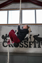 young girl climbs the rope in the crossfit room