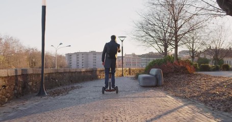 Business man riding segway in city commuting to work or home while calling using smartphone.Modern future transport technology.Sidewalk urban outdoor.Warm sunset backlight.4k slow motion 60p video