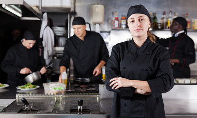 Confident female chef with a team of cooks in restaurant kitchen