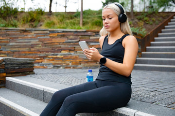 Beautiful sports woman sitting at stairs listen to music from smartphone