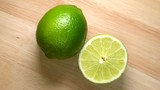 Whole lime and half rotating top view on wooden background