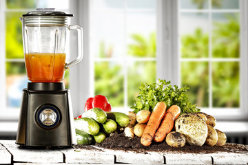 Blender in kitchen on wooden table with white window and fresh vegetables 