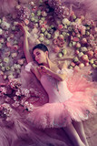 Thinking. Top view of beautiful young woman in pink ballet tutu surrounded by flowers. Spring mood and tenderness in coral light. Art photo. Concept of spring, blossom and nature's awakening.