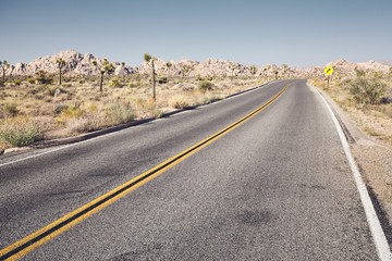 Retro toned picture of a desert road, front focus on asphalt, USA.