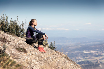 Trail runner sitting and taking a break while looking landscape from mountain peak.