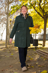 Senior woman with maple leaves walks in autumn park