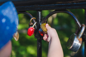 The hands of a small child hold a love lock fastened to the railings of the bridge
