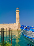 Rethymno port lighthouse and white blue boat. Bright summer day.