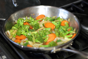 Stir fried vegetables cooking in a stainless steel pan.